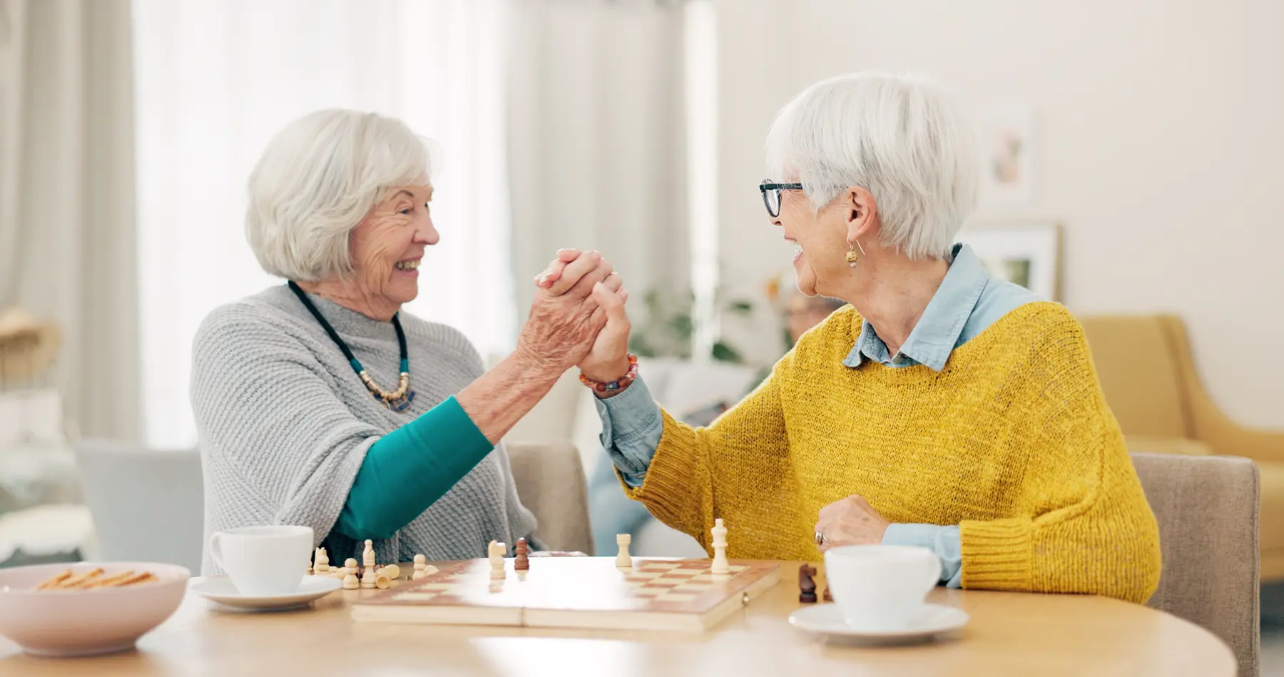 Senior woman, friends and high five for chess match, game or winning on table together at home. Happy elderly women in celebration, playing strategic board game for victory or checkmate in retirement.