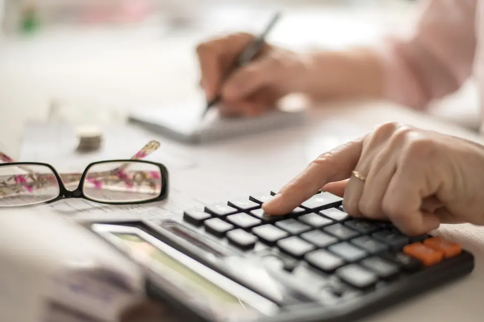 A senior woman is taking a note while using a calculator / Une femme âgée prend des notes tout en utilisant une calculatrice