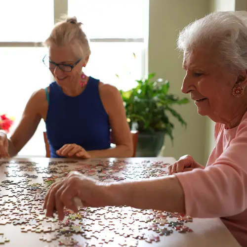 Senior woman and her adult daughter are having a fun time together, solving jigsaw puzzle / Une femme âgée et sa fille adulte s'amusent ensemble en faisant un puzzle.