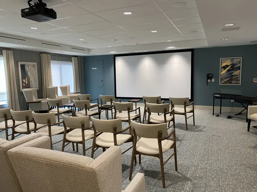 Theatre room with rows of chairs and large projection screen at Chartwell Riverstone / Salle de cinéma avec rangées de chaises et grand écran de projection à Chartwell Riverstone