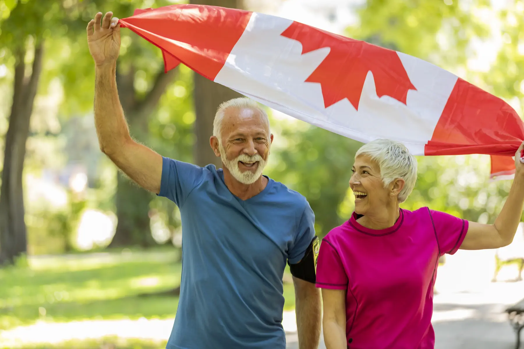 Senior couple is holding Canadian flag up in the air / Un couple d'aînés tient le drapeau canadien en l'air.