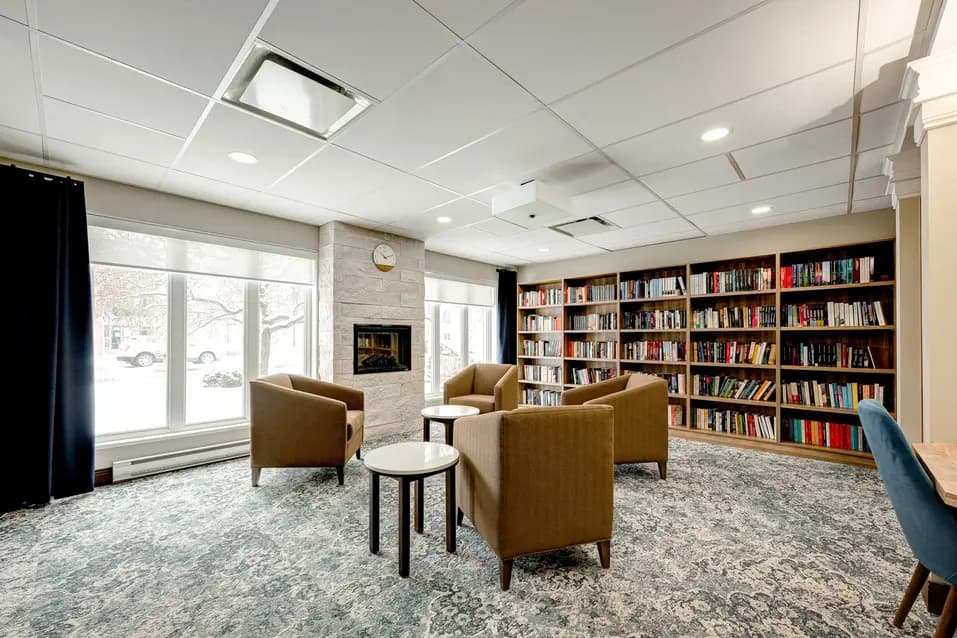 Bibliothèque avec étagères et foyer à Chartwell Oasis St-Jean / Library with bookshelves and fireplace at Chartwell Oasis St-Jean