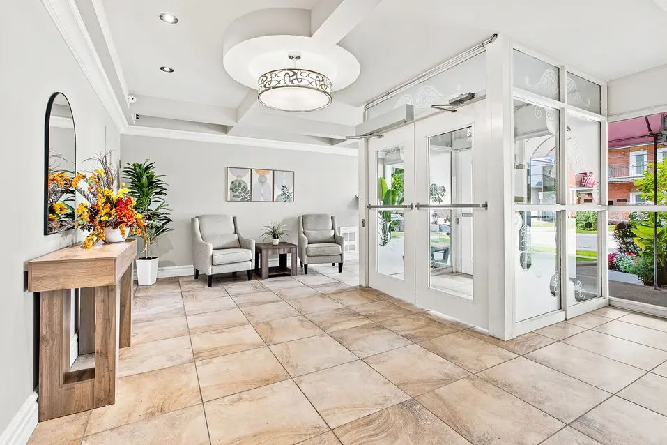 Hall d’entrée lumineux avec portes vitrées et coin salon au Chartwell Domaine Notre-Dame. / Bright entrance lobby with glass doors and seating area at Chartwell Domaine Notre-Dame.