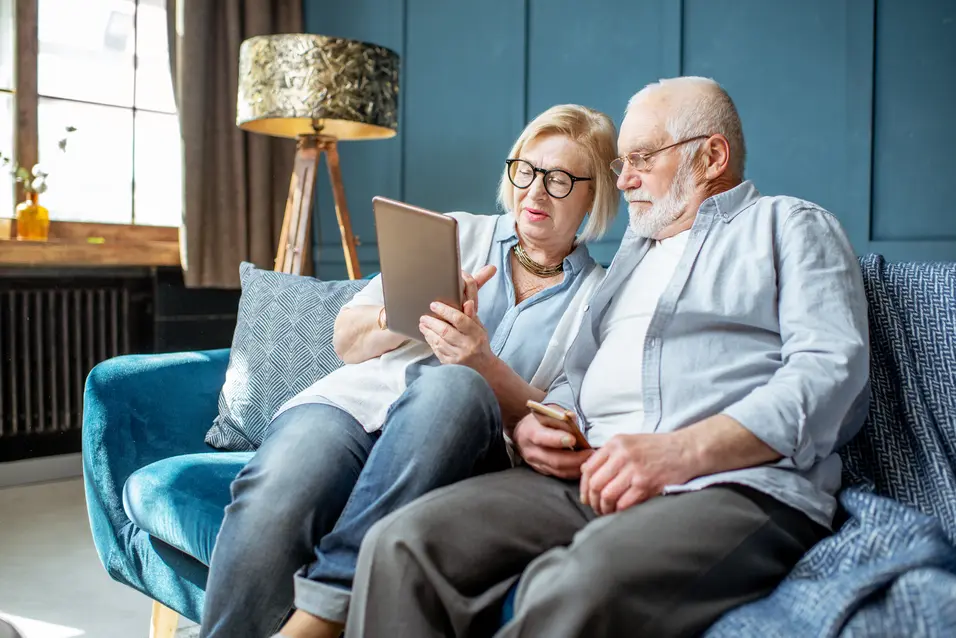 Older adults reviewing information together on a tablet while seated in a living room. / Personnes âgées consultant de l’information ensemble sur une tablette dans un salon.