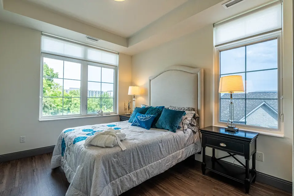 Chartwell Palermo Village model suite. This room has two large windows a bed and side table.