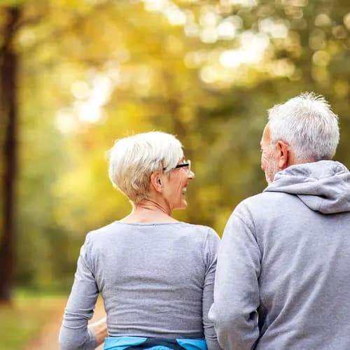 Older adults walking together on a tree-lined trail in a park. / Personnes âgées marchant ensemble sur un sentier bordé d’arbres dans un parc.