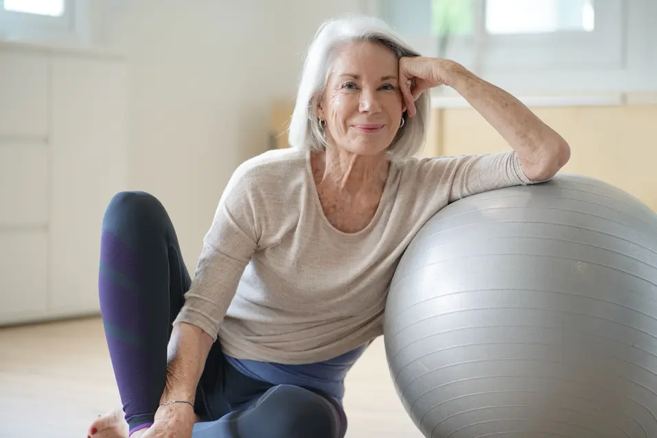 Older adult seated beside an exercise ball in a fitness and wellness space. / Personne âgée assise à côté d’un ballon d’exercice dans un espace de santé et de mieux-être.