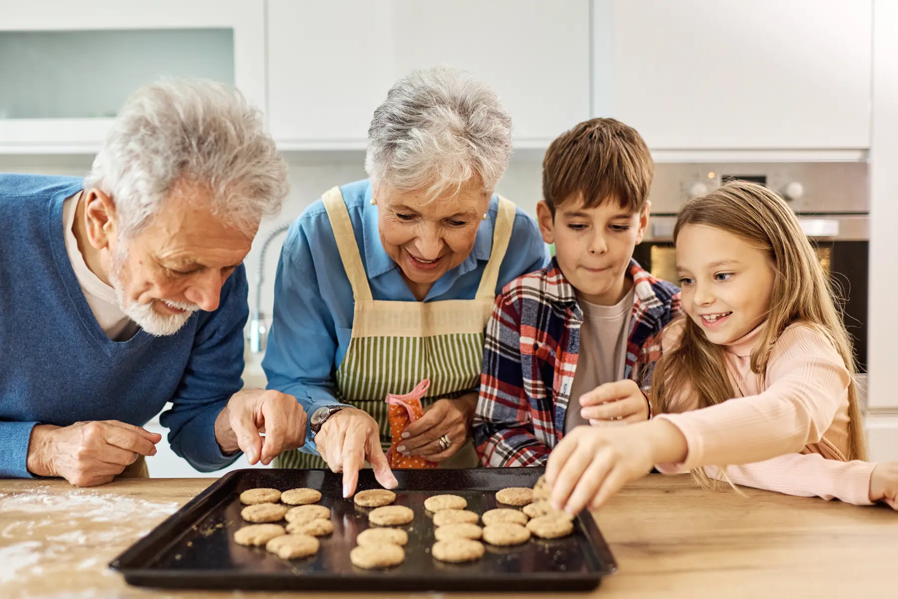 seniorcouplewithgrandsonandgranddaughterbakingcookiestogether.