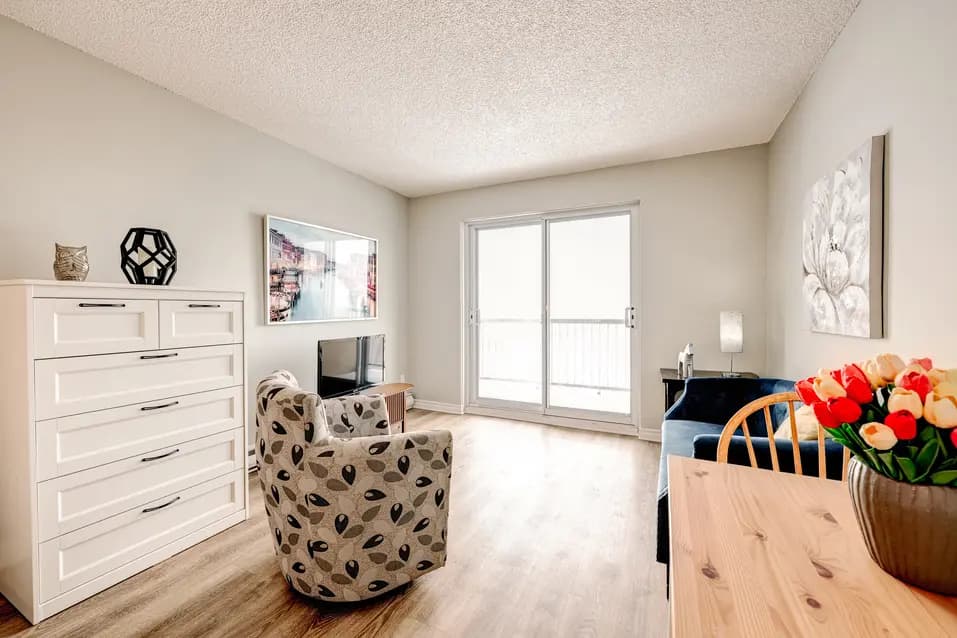 Petit salon lumineux avec fauteuil, commode et balcon à Les Écores / Bright small living room with armchair, dresser, and balcony at Les Écores