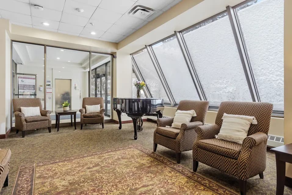 Lounge with wide tilted windows, grand piano and couches at Chartwell McConnell / Salon avec de larges fenêtres inclinées, un piano à queue et des canapés chez Chartwell McConnell