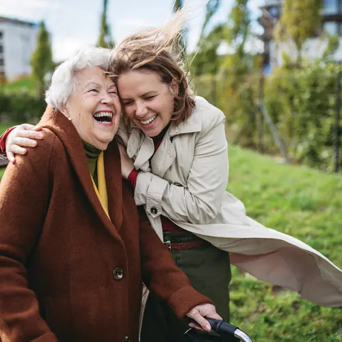 Senior woman and her adult daughter smiling big while having a walk during a windy day / Une femme âgée et sa fille adulte sourient largement pendant une promenade par une journée venteuse