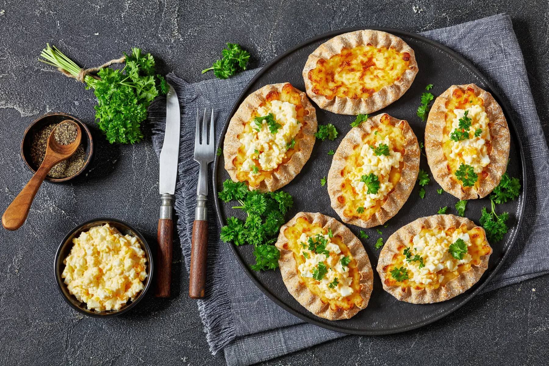 Karelian pasties, karelian pies, pirogs, karjalanpiirakka, classic Finnish pastries of thin rye crust with rice filling, topped with butter mixed with chopped-up boiled eggs on plate, flat lay