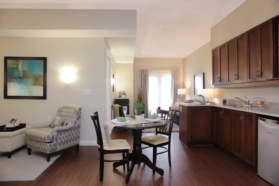 Spacious model suite featuring a dining area and dark wood cabinetry at Chartwell Dorchester Terrace / Suite modèle spacieuse comprenant un coin repas et des armoires sombres à Chartwell Dorchester Terrace