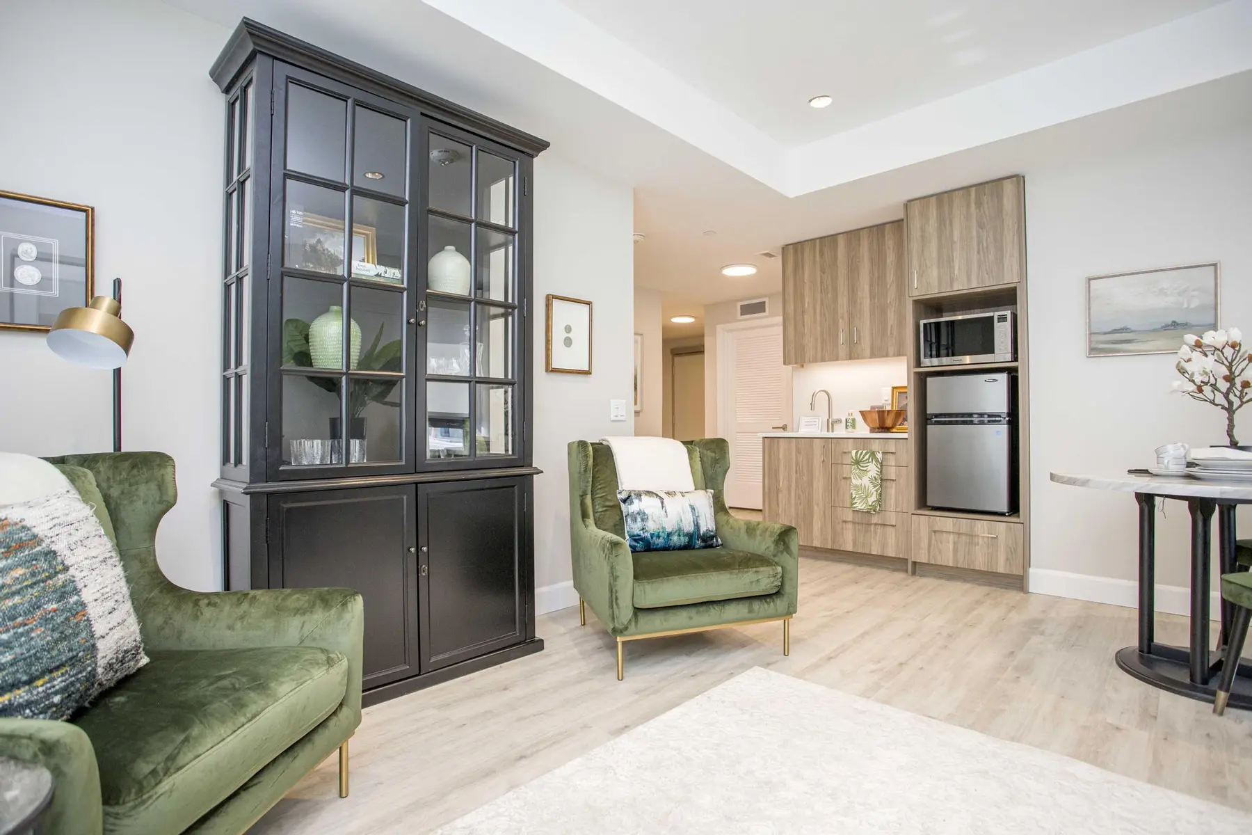Bright suite living area with green accent chairs and kitchenette at Chartwell Riverstone / Aire de vie lumineuse avec fauteuils verts et cuisinette à Chartwell Riverstone