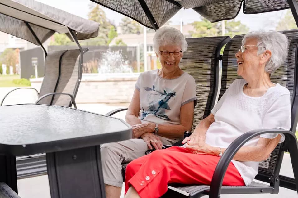 Chartwell senior residents chatting outside in lounge chair / Les résidents seniors de Chartwell discutent dehors, confortablement installés dans des fauteuils
