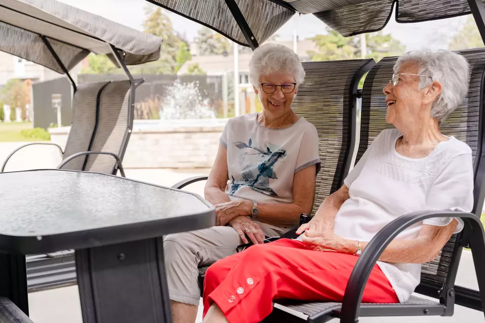 Two senior women are sitting on a swing chair and having fun conversation / Deux femmes âgées sont assises sur une balançoire et ont une conversation amusante