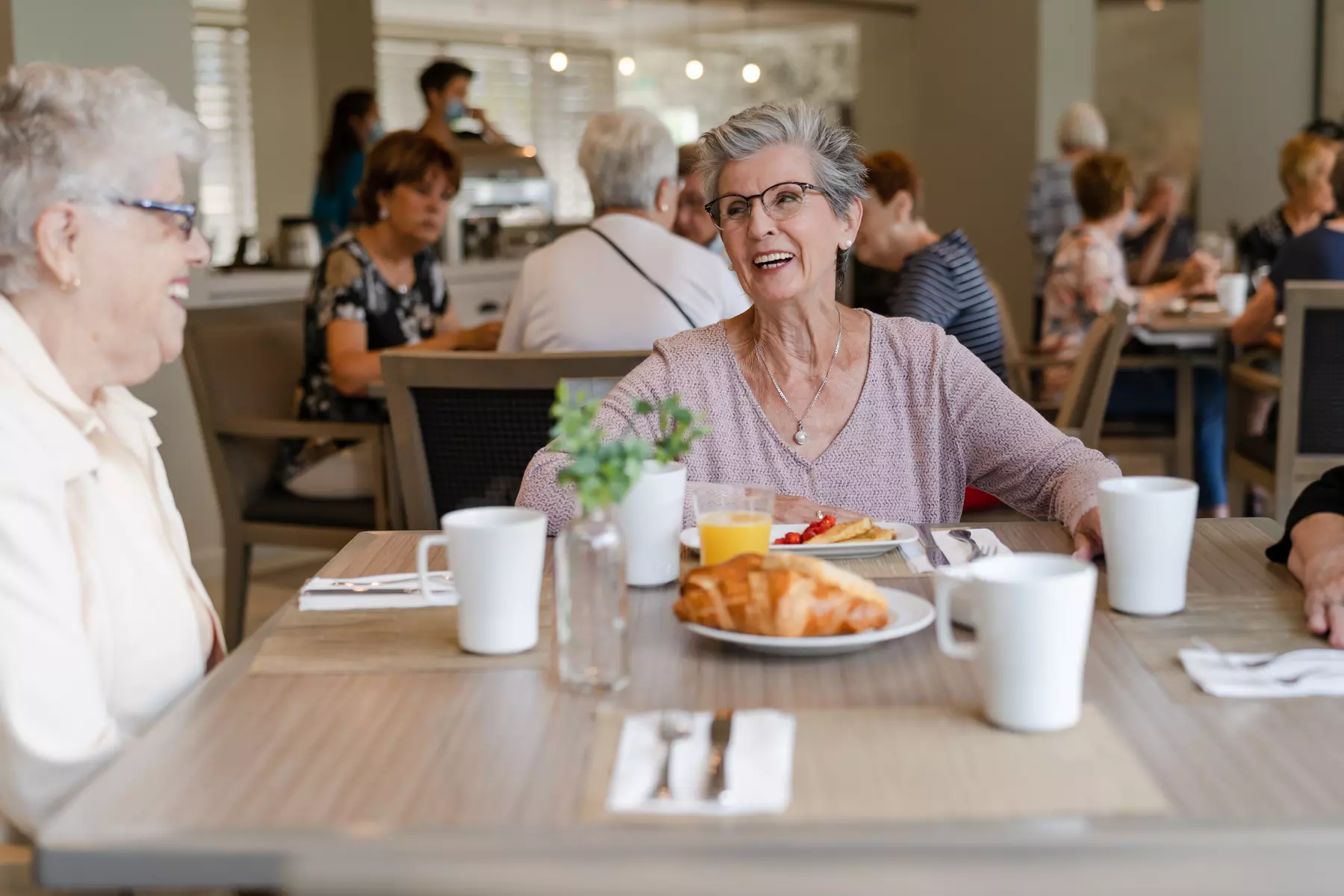 Senior residents having a pleasant conversation at the dinning table while enjoying a cup of coffee with croissant