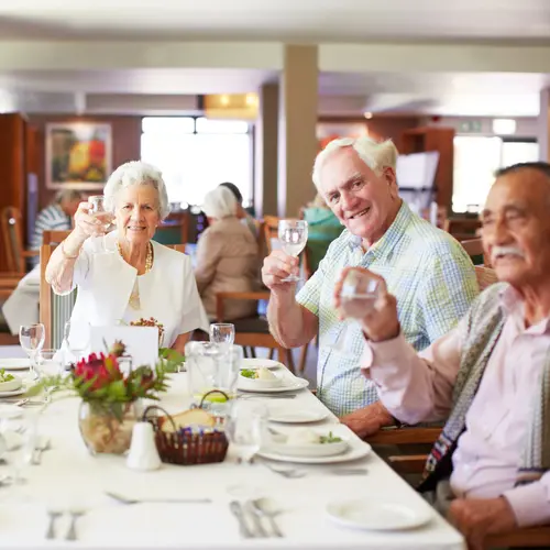 A group of seniors are tossing their drinks with bright smiles at a dining table / Un groupe de personnes âgées se jette sur leurs boissons avec des sourires éclatants autour d'une table à manger.