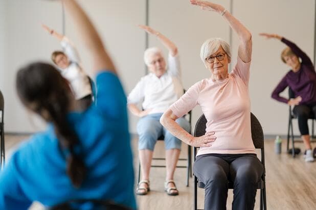 Senior residents performing chair yoga on chair with the instructor / Résidents seniors pratiquant le yoga sur chaise avec leur instructeur