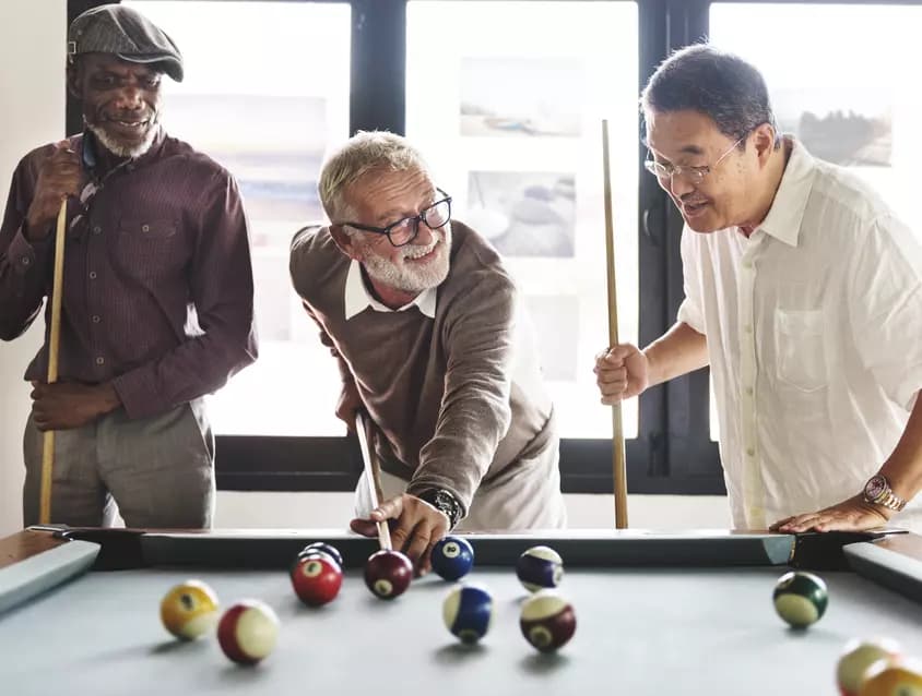 Three senior men are enjoying playing pool together / Trois seniors s'amusent à jouer au billard ensemble
