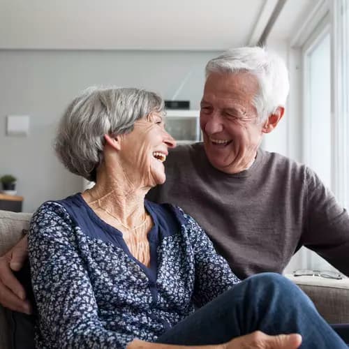 Senior couple in a couch happily laughing while looking into each others' eye / Couple de seniors dans un canapé, riant joyeusement en se regardant dans les yeux