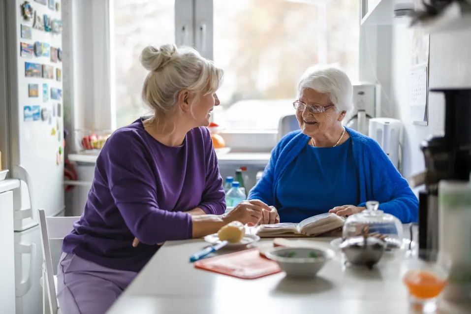 Senior woman and her adult daughter are reading a book at the tea table / Une femme âgée et sa fille adulte lisent un livre à la table de thé
